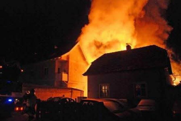 Ein Haus steht in Flammen, während Feuerwehrleute im Vordergrund zu sehen sind.