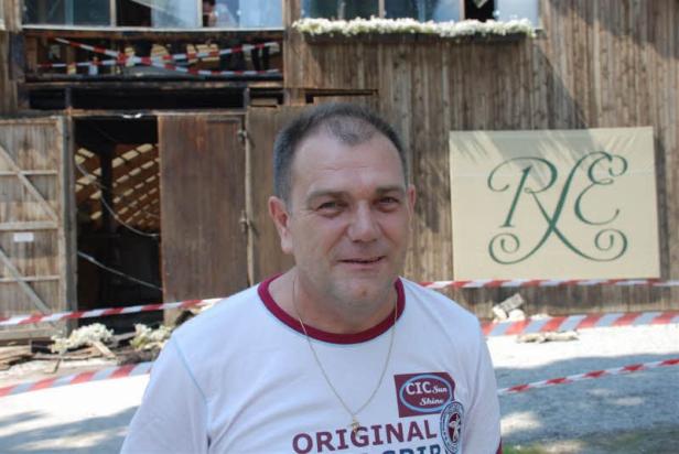 Ein Mann steht vor einem beschädigten Gebäude mit einem Logo an der Wand.