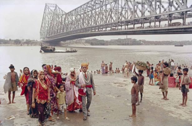 Eine Hochzeitsgesellschaft geht am Ufer des Flusses unter der Howrah-Brücke in Kalkutta entlang.