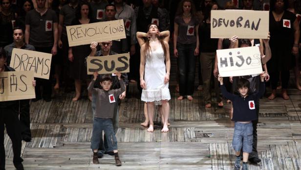 Eine Gruppe von Menschen, darunter Kinder, hält Schilder mit Aufschriften wie „Revoluciones“ und „Hijos“.