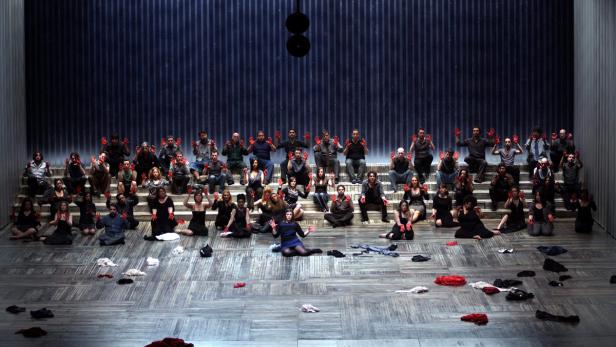 Eine Theaterinszenierung mit einer Gruppe von Menschen, die rote Farbe auf ihren Händen haben.