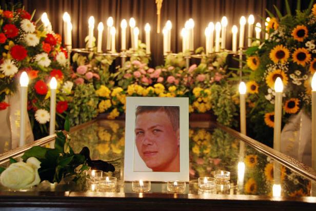 Ein Porträtfoto eines jungen Mannes auf einem Sarg, umgeben von Blumen und Kerzen.