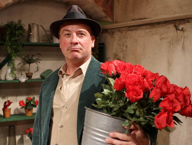 Ein Mann mit Hut hält einen Eimer mit roten Rosen.