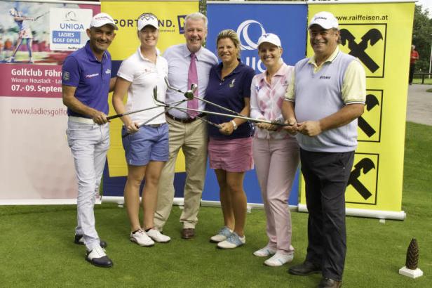 Eine Gruppe von Personen posiert mit Golfschlägern vor Bannern des Ladies Golf Open.
