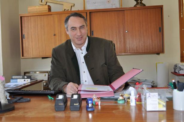 Ein Mann in Trachtenjacke sitzt an einem Schreibtisch mit Aktenordnern.