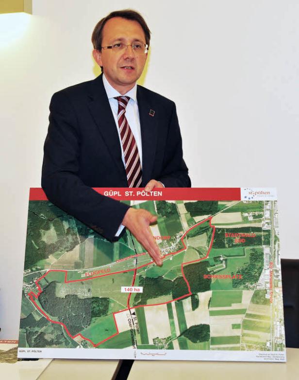 Ein Mann im Anzug präsentiert einen Plan von St. Pölten, der ein Flugfeld und ein Schiessplatz zeigt.