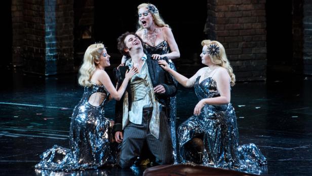 BREGENZER FESTSPIELE 2015: FOTOPROBE "HOFFMANNS ER Ein Mann wird auf einer Bühne von drei Frauen in glitzernden Kleidern umringt.