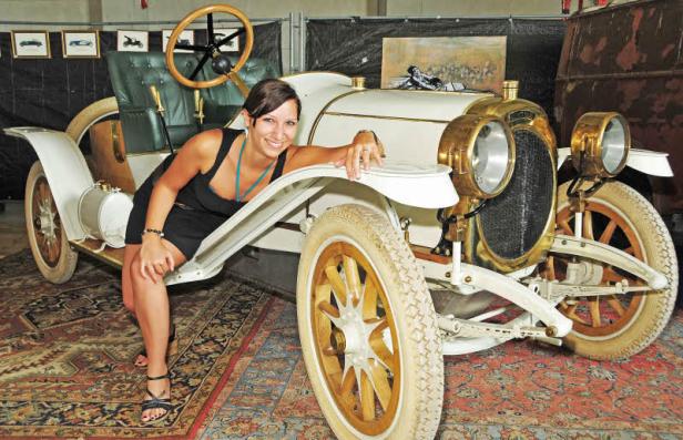 Eine Frau posiert an einem Oldtimer mit goldenen Scheinwerfern.