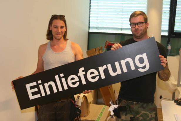 Zwei Männer halten ein Schild mit der Aufschrift „Einlieferung“.