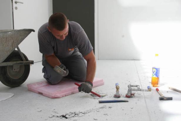 Ein Bauarbeiter stemmt mit einem Meißel Fliesen auf einem Fußboden auf.