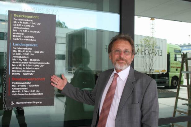 Ein Mann im Anzug steht vor dem Justizzentrum Korneuburg und zeigt auf die Öffnungszeiten.
