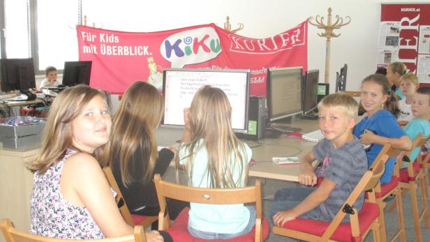 Eine Gruppe Kinder sitzt an Computern unter einem „Kiku Kurier“-Banner.