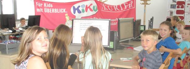 Eine Gruppe Kinder sitzt an Computern unter einem „KiKu Kurier“-Banner.