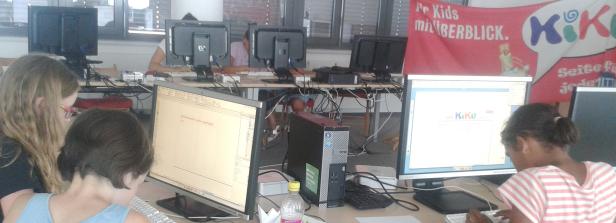 Kinder arbeiten an Computern in einem Raum mit einem „KiKu“-Banner.