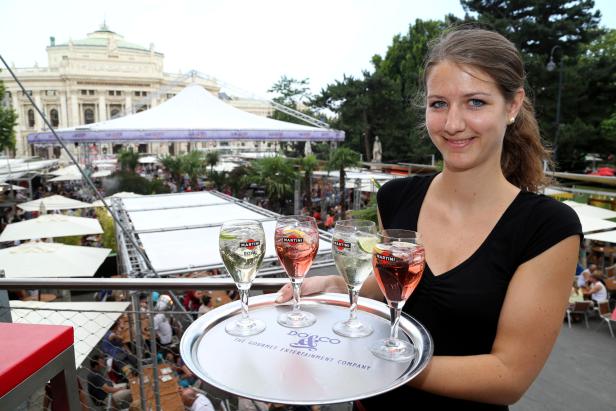 Eine Kellnerin serviert vier Gläser Martini Royal auf einem Tablett vor dem Burgtheater in Wien.