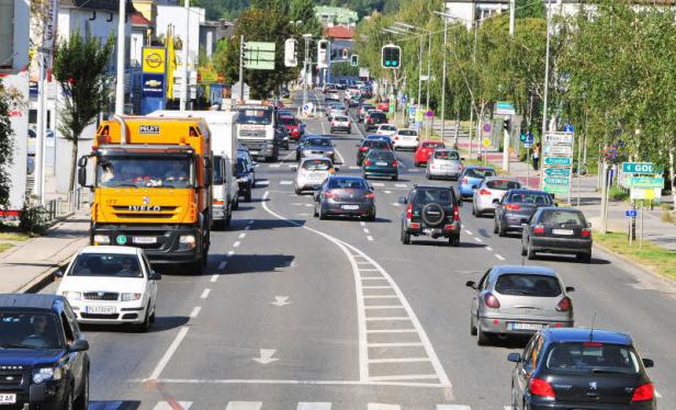 Eine belebte Straße mit vielen Autos und einem orangefarbenen LKW im Vordergrund.