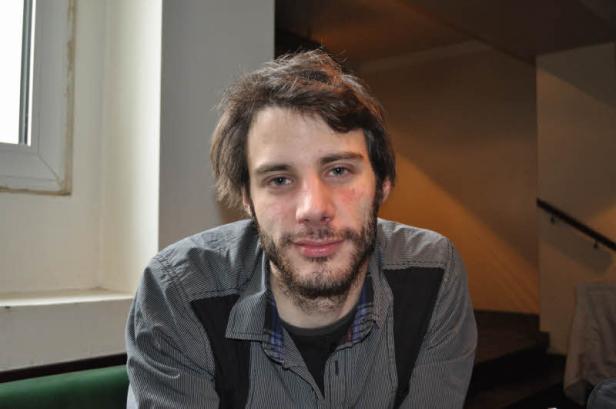 Ein junger Mann mit Bart und gestreiftem Hemd schaut in die Kamera.