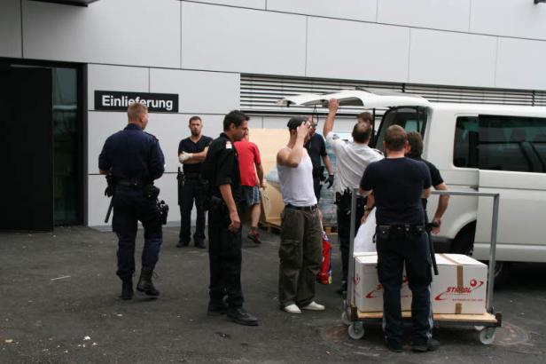 Polizisten beobachten, wie Männer Kartons aus einem Lieferwagen entladen.