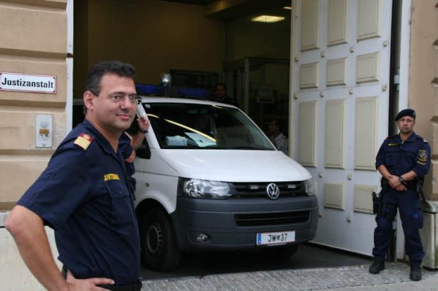 Zwei Justizbeamte stehen vor einem weißen Transporter der Justizanstalt.