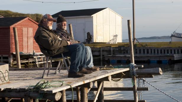 Zwei ältere Männer sitzen auf einem Pier und blicken aufs Meer.