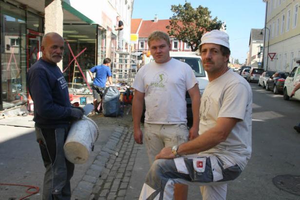 Drei Bauarbeiter posieren auf einer Straße vor einem Gebäude.