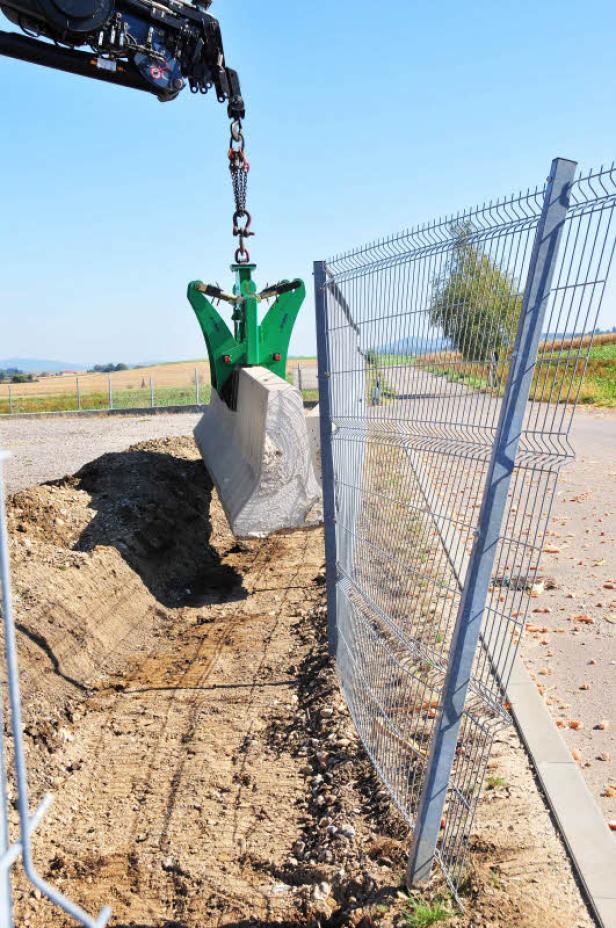 Ein Kran platziert einen Betonblock neben einem Zaun.