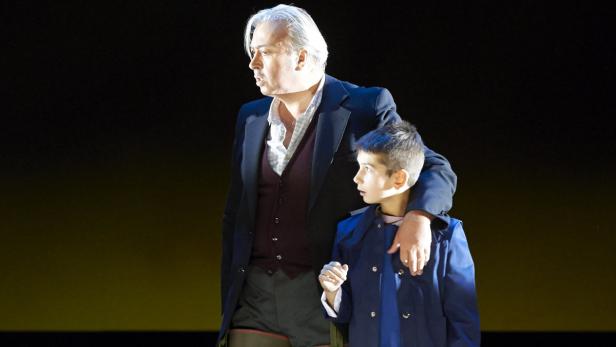 Ein Mann im Anzug legt einem Jungen im Mantel den Arm um die Schulter.