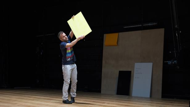 Ein Mann hält eine gelbe Tafel auf einer Bühne hoch.