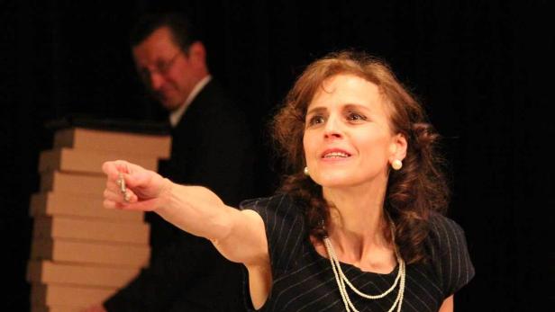 Eine Frau hält einen Schlüssel hoch, im Hintergrund ein Mann und ein Stapel Kartons.