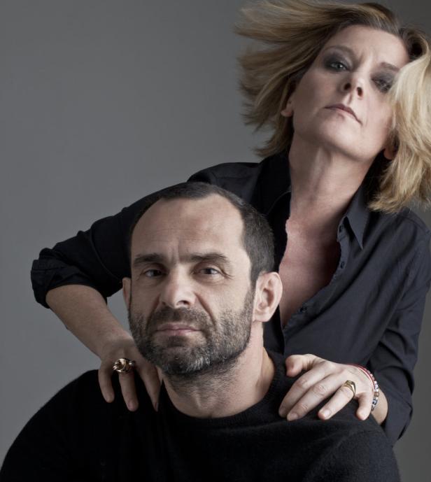 Ein Mann und eine Frau posieren vor einem grauen Hintergrund.