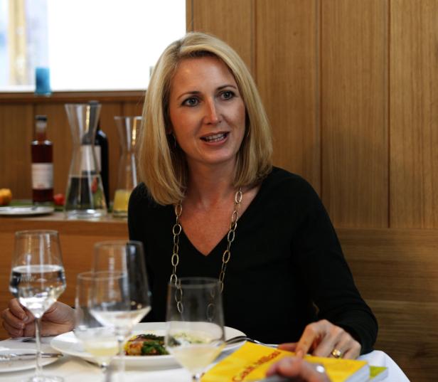 Eine blonde Frau sitzt an einem gedeckten Tisch in einem Restaurant.