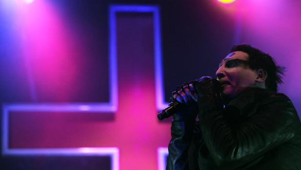 Marilyn Manson singt vor einem großen, leuchtenden Kreuz.