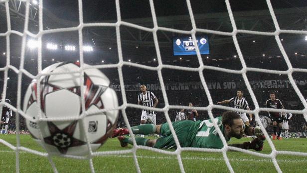 Ein Fußball liegt im Netz, während der Torwart auf dem Rasen liegt.