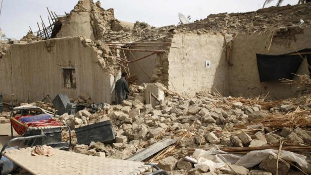 Survivors of an earthquake walk on rubble of a mud Ein Mann steht vor einem durch ein Erdbeben zerstörten Haus.