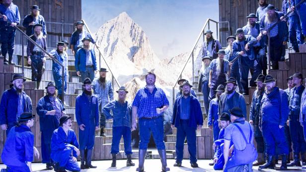 Eine Gruppe von Männern mit Bärten steht auf einer Bühne vor einem Bergkulisse.