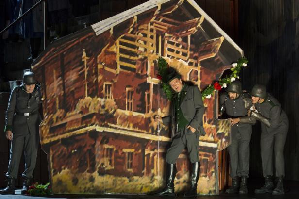 Szene aus einer Theateraufführung mit Schauspielern vor einem bemalten Haus.