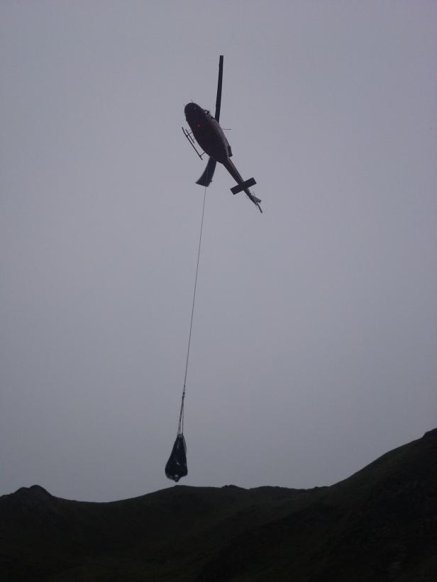 Ein Hubschrauber transportiert eine Last über eine hügelige Landschaft.