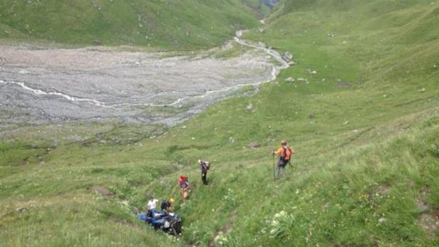 Eine Gruppe von Wanderern quert einen grünen Berghang.