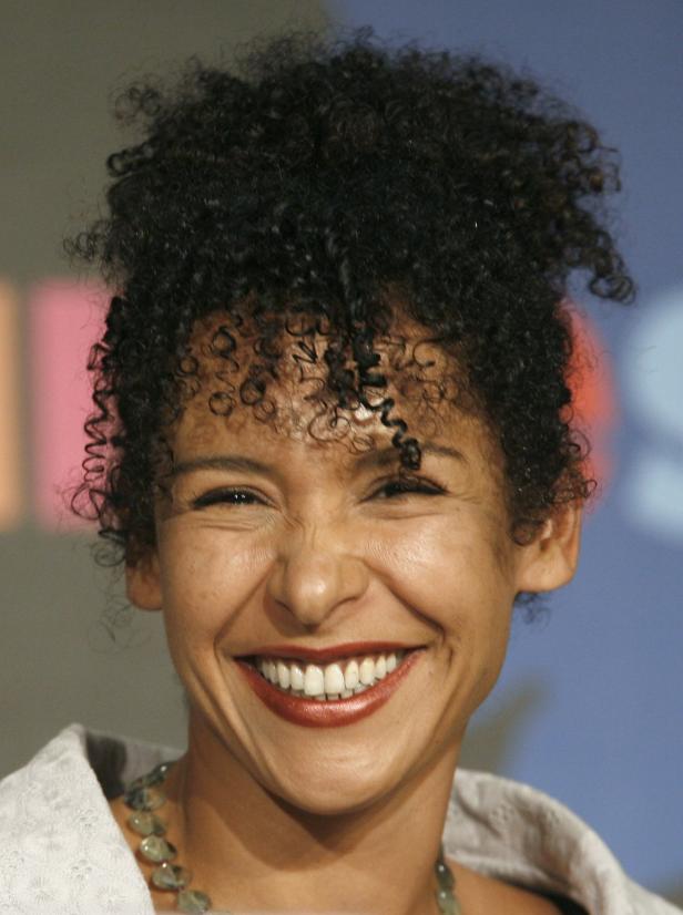Eine lachende Frau mit lockigem Haar und einer Halskette.