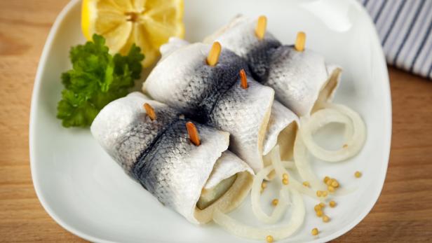 Ein Teller mit Rollmops, garniert mit Zwiebeln, Senfsaat, Zitrone und Petersilie.