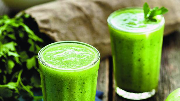 Zwei Gläser mit grünem Smoothie stehen auf einem Holztisch.