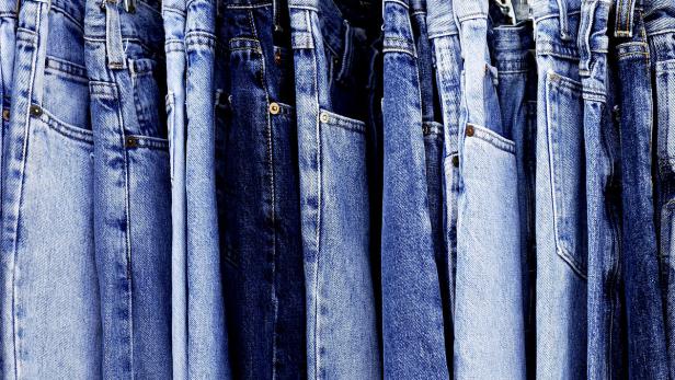 Eine Reihe von Jeanshosen in verschiedenen Blautönen hängen an einer Stange.