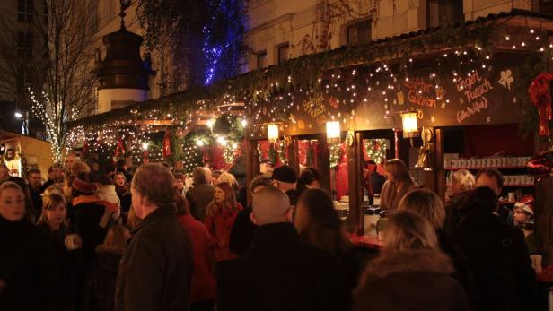 Menschen besuchen einen Weihnachtsmarkt mit Ständen, die mit Lichtern und Dekorationen geschmückt sind.