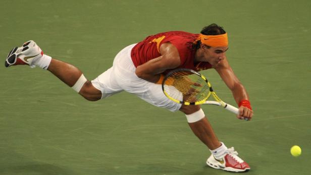 Rafael Nadal schlägt einen Tennisball auf einem grünen Platz.