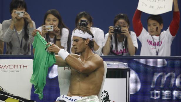 Rafael Nadal sitzt erschöpft auf einem Stuhl und hält ein grünes T-Shirt hoch.