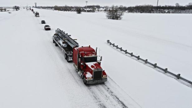 Ein roter Lastwagen transportiert Stahlträger auf einer schneebedeckten Straße.