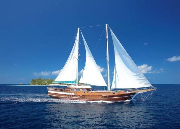 Ein hölzernes Segelboot fährt auf dem blauen Ozean an einer tropischen Insel vorbei.