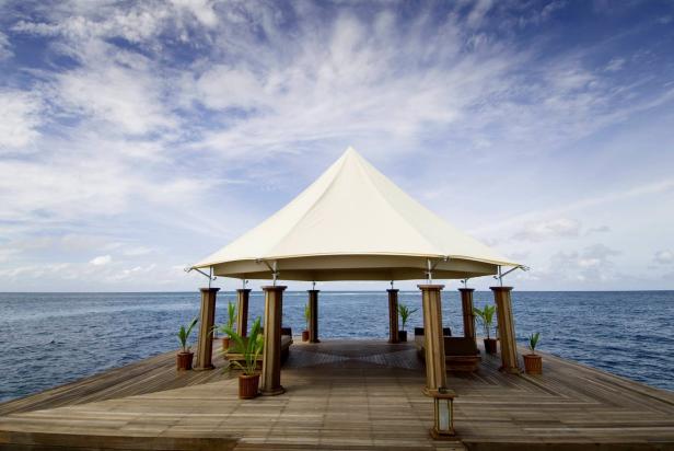 Ein Pavillon mit Liegen steht auf einem Holzsteg über dem Meer.