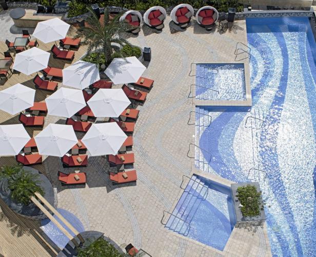 Luftaufnahme eines Pools mit Liegestühlen und Sonnenschirmen.