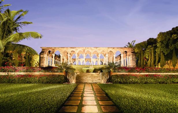 Die Ruinen eines Gebäudes mit Bögen und Säulen in einem gepflegten Garten.